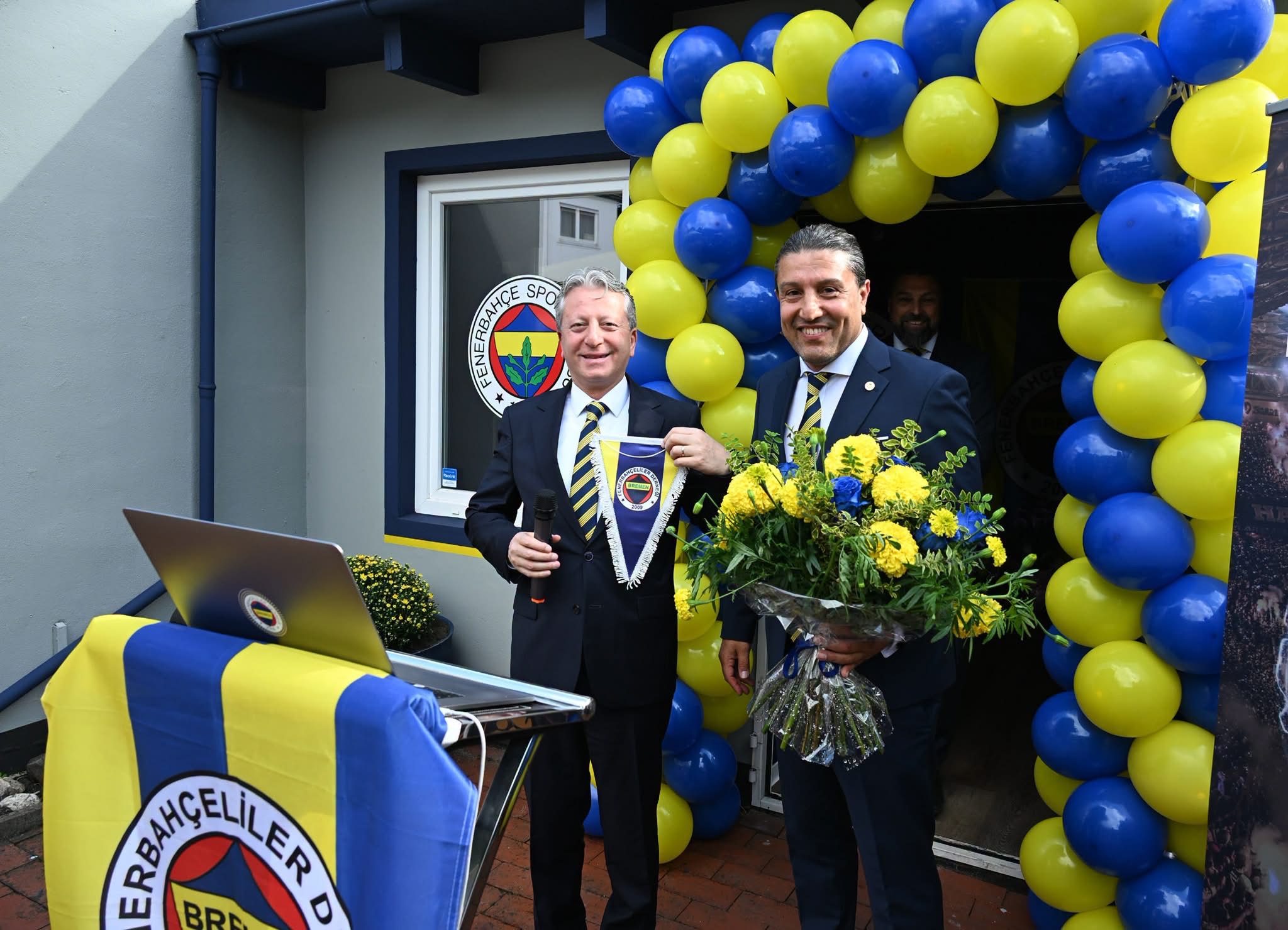 İlhan Şükrü Güven überreicht Yusuf Arıkan ein Vereinsgeschenk und einen gelb-blauen Blumenstrauß.